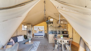 Un alojamiento tipo tienda de campaña acogedor, con cama, sofá, zona de comedor y kitchenette.