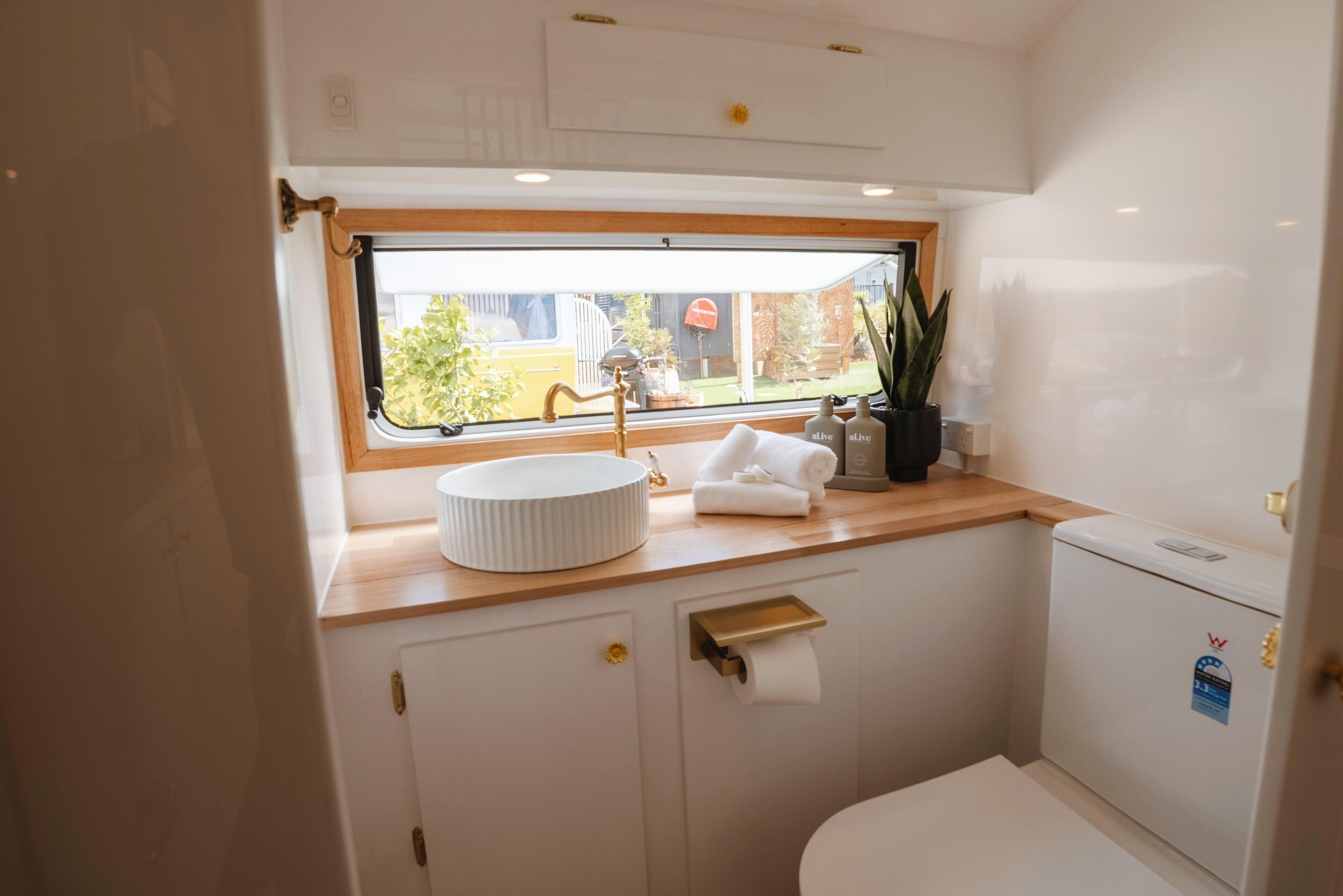 A compact bathroom with a window, a sink, a toilet, and a small cabinet.