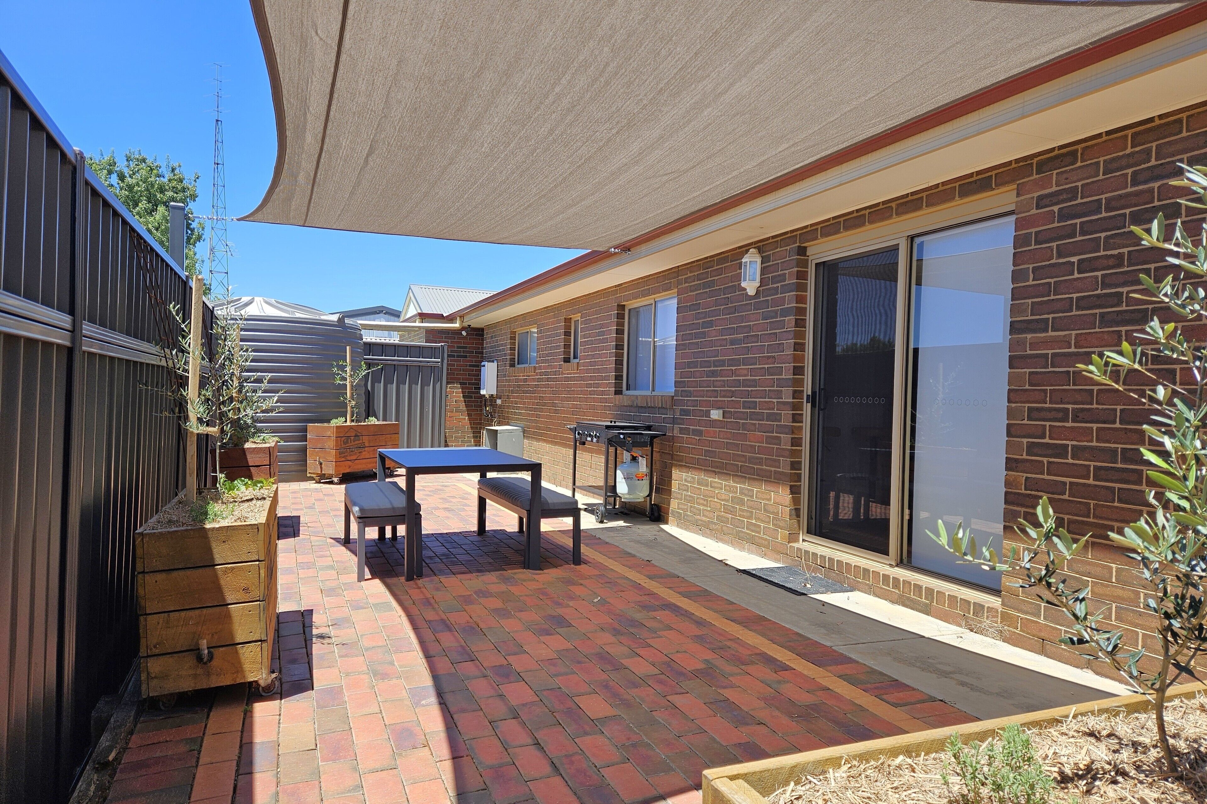 Un patio trasero con una terraza, una mesa y una parrilla.
