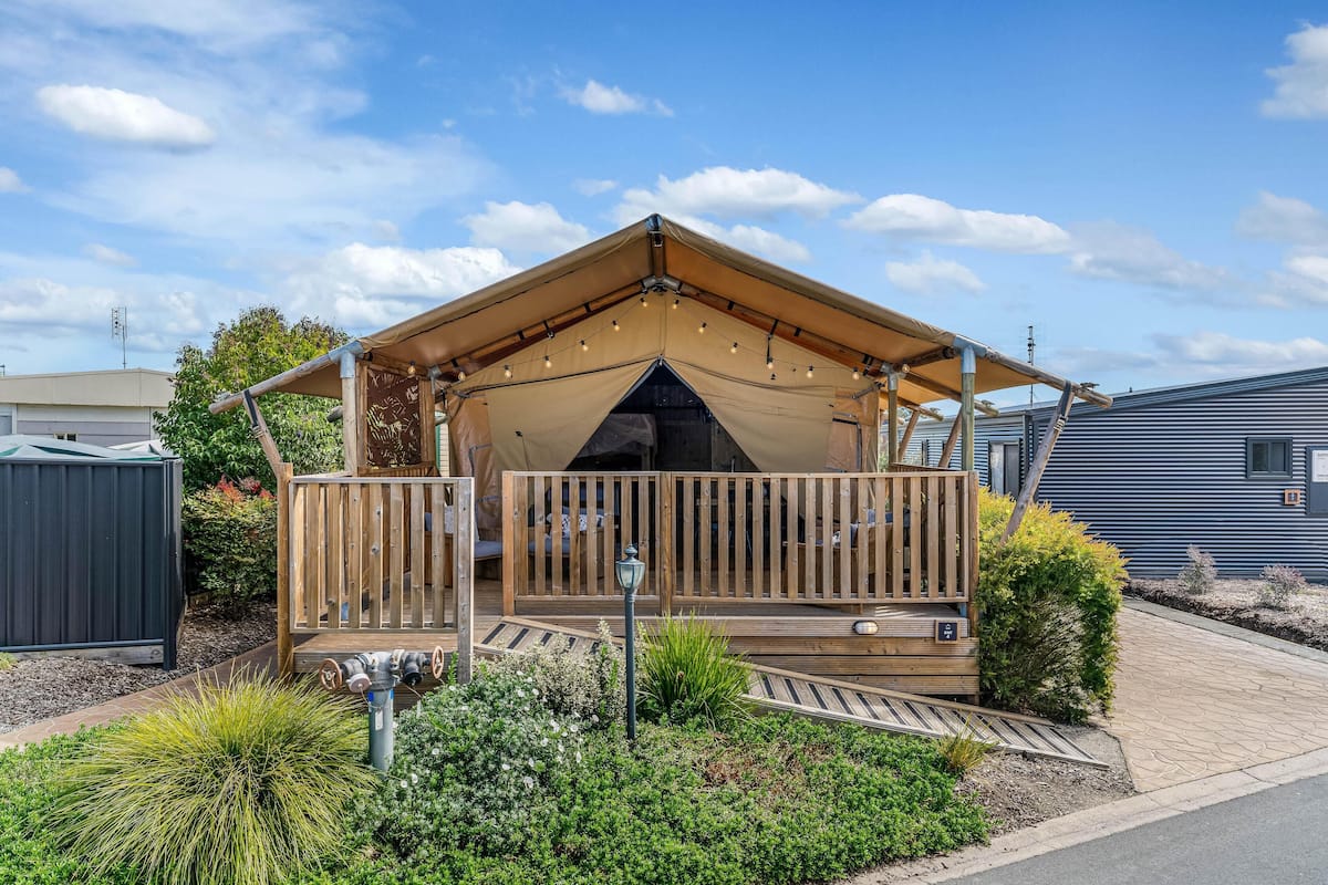 Eine Holzterrasse mit überdachtem Sitzbereich, umgeben von angelegten Gartenbeeten und einer kleinen Außenleuchte.