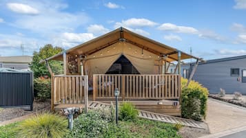 A wooden deck with a covered seating area, surrounded by landscaped garden beds and a small outdoor light fixture.