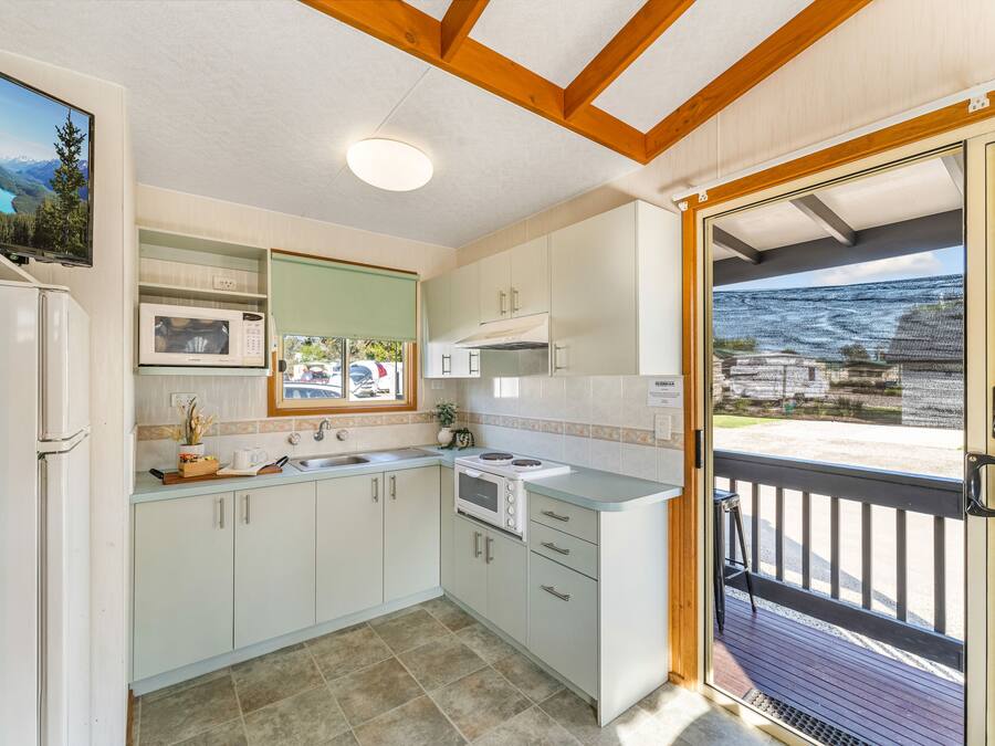 A modern kitchen with white cabinets, a microwave, and a stove. There is a window with a view of a mountain and a lake.