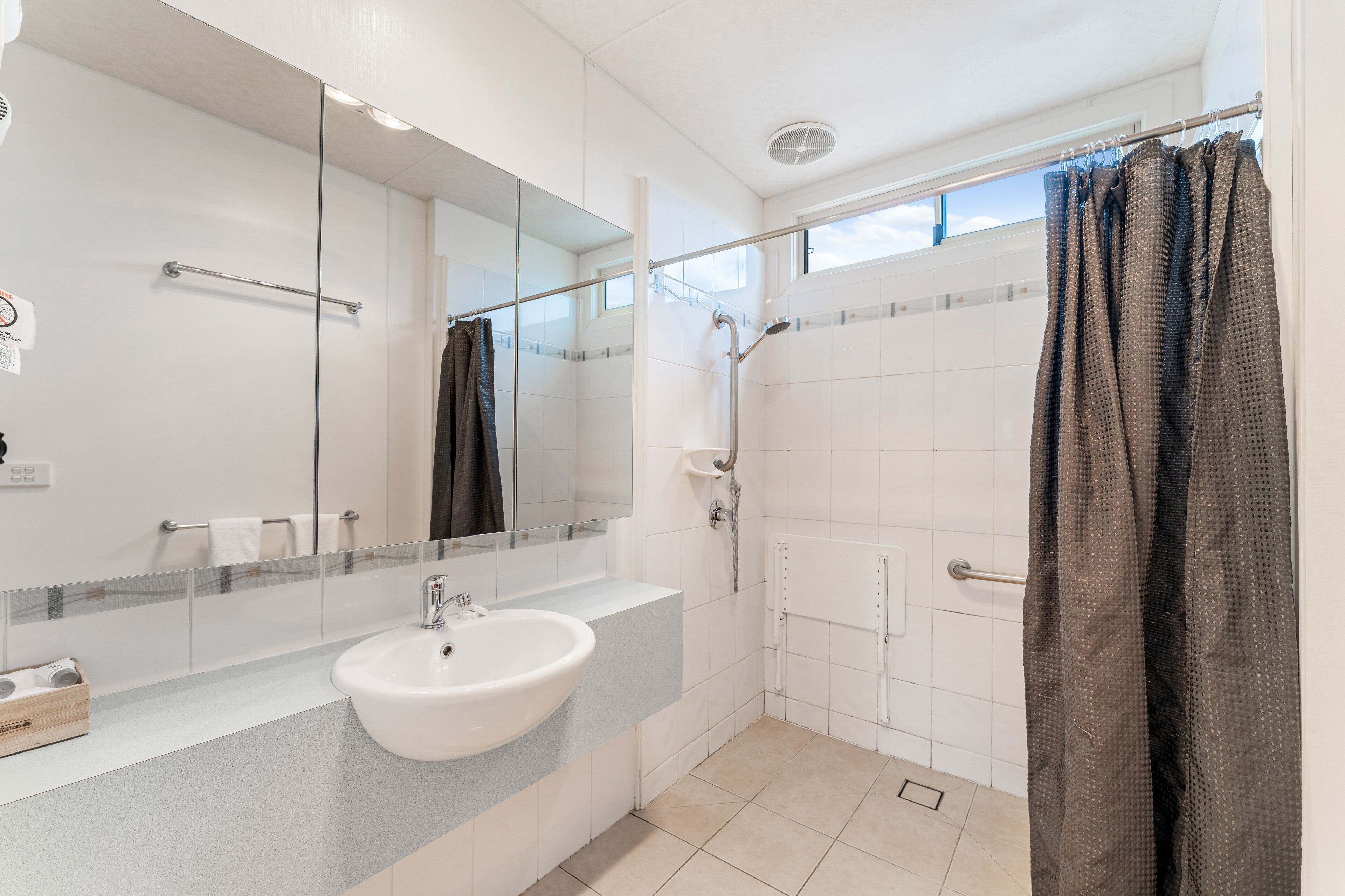 Ein modernes Badezimmer mit einem großen Spiegel, einem Waschbecken, einer Dusche und einem Fenster.