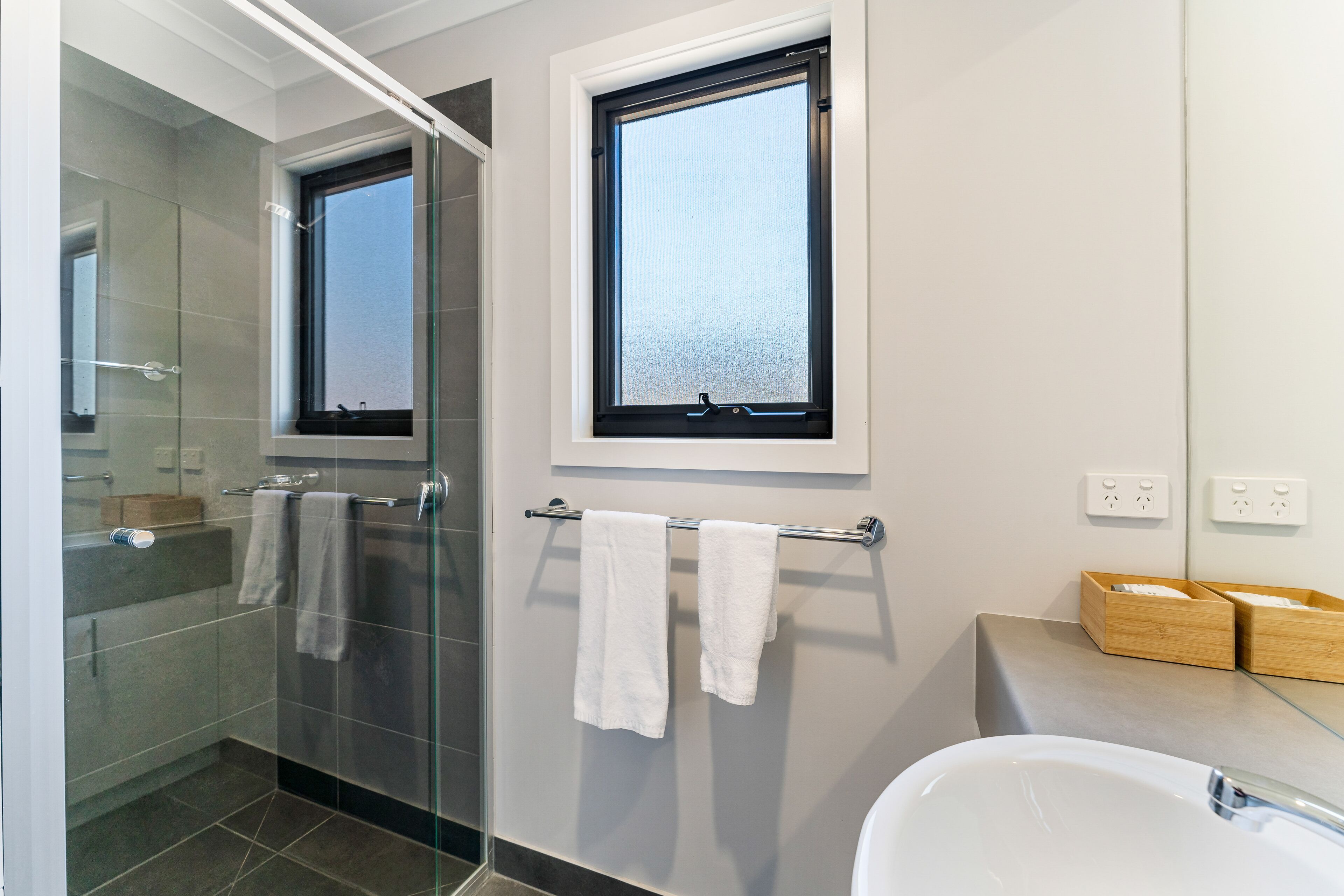 A modern bathroom with a glass shower enclosure, a bathtub, and a window above the sink.