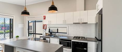 Une cuisine moderne avec des meubles blancs, des appareils en acier inoxydable et un îlot central doté de tabourets de bar.