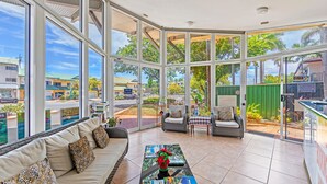 A spacious room with large windows, a sofa with patterned cushions, a coffee table with a decorative item, and a view of the outside. - Koala Court Holiday Apartments (Cairns North)