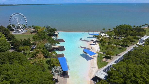 An aerial view of a resort with a large body of water, a Ferris wheel, and a beach area with structures and greenery. - Koala Court Holiday Apartments (Cairns North)