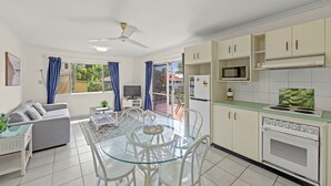 A modern kitchen with white cabinets, a microwave, and a stove. There is a dining area with a glass table and chairs. - Koala Court Holiday Apartments (Cairns North)