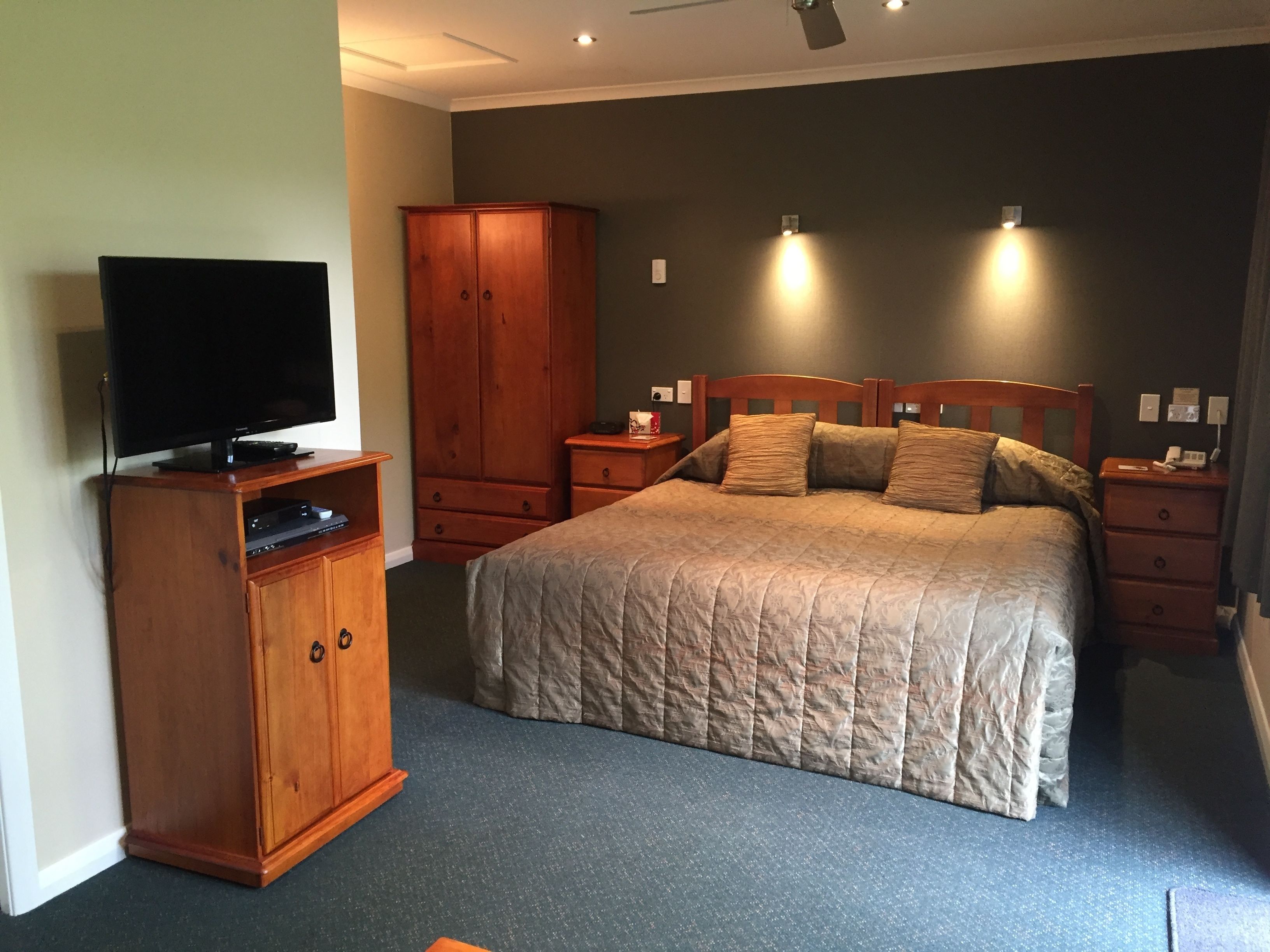 Une chambre à coucher avec un lit, un téléviseur posé sur un meuble en bois, une armoire et des lampes de chevet.