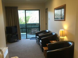 Habitación de hotel con zona de estar, televisión, lámpara y puerta corrediza de vidrio que da a un espacio exterior.