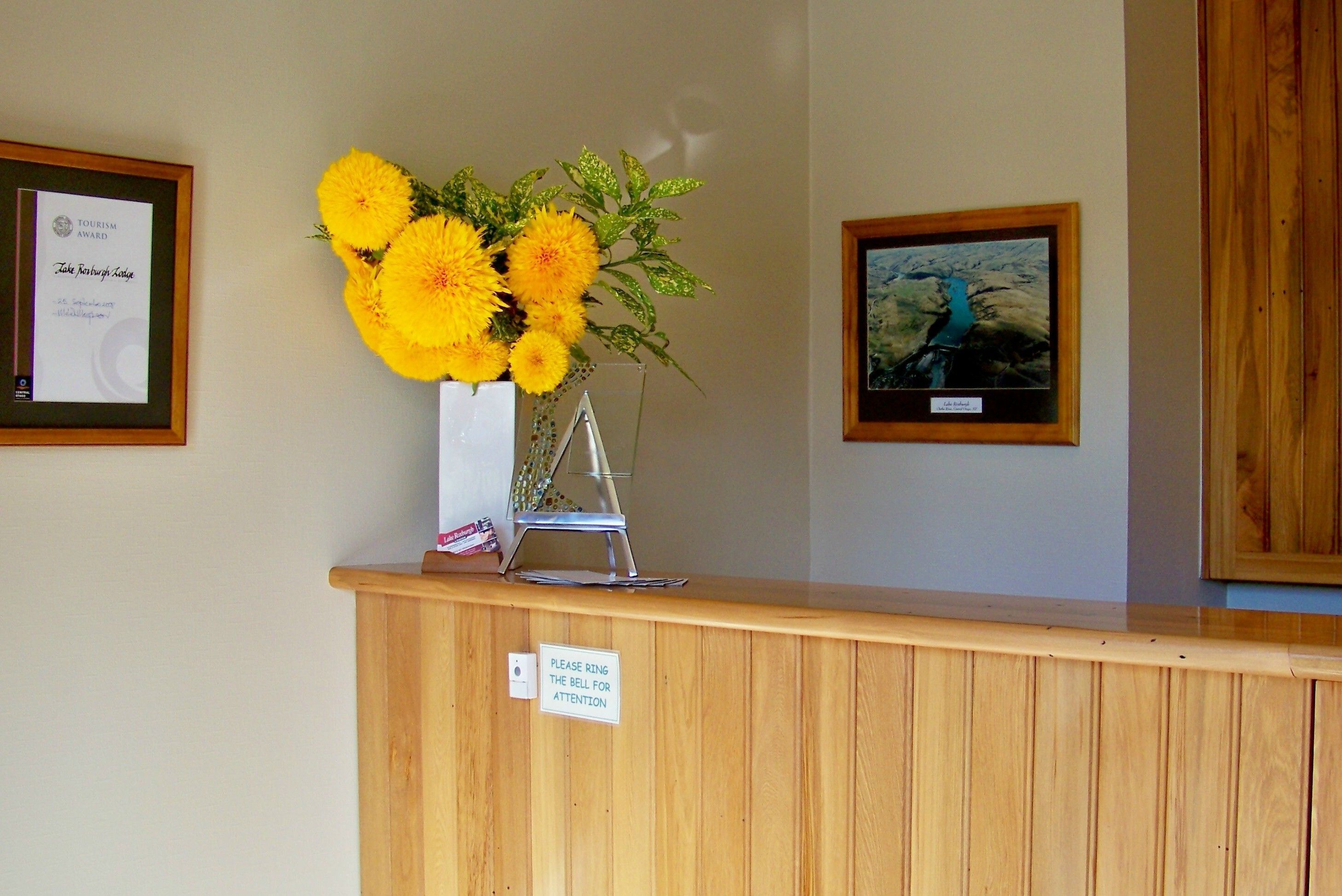 A reception desk with a framed award, a vase of yellow flowers, and a framed landscape painting.