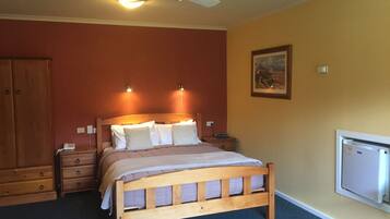 A bedroom with a wooden bed, two bedside tables, a ceiling fan, and a wall-mounted TV.