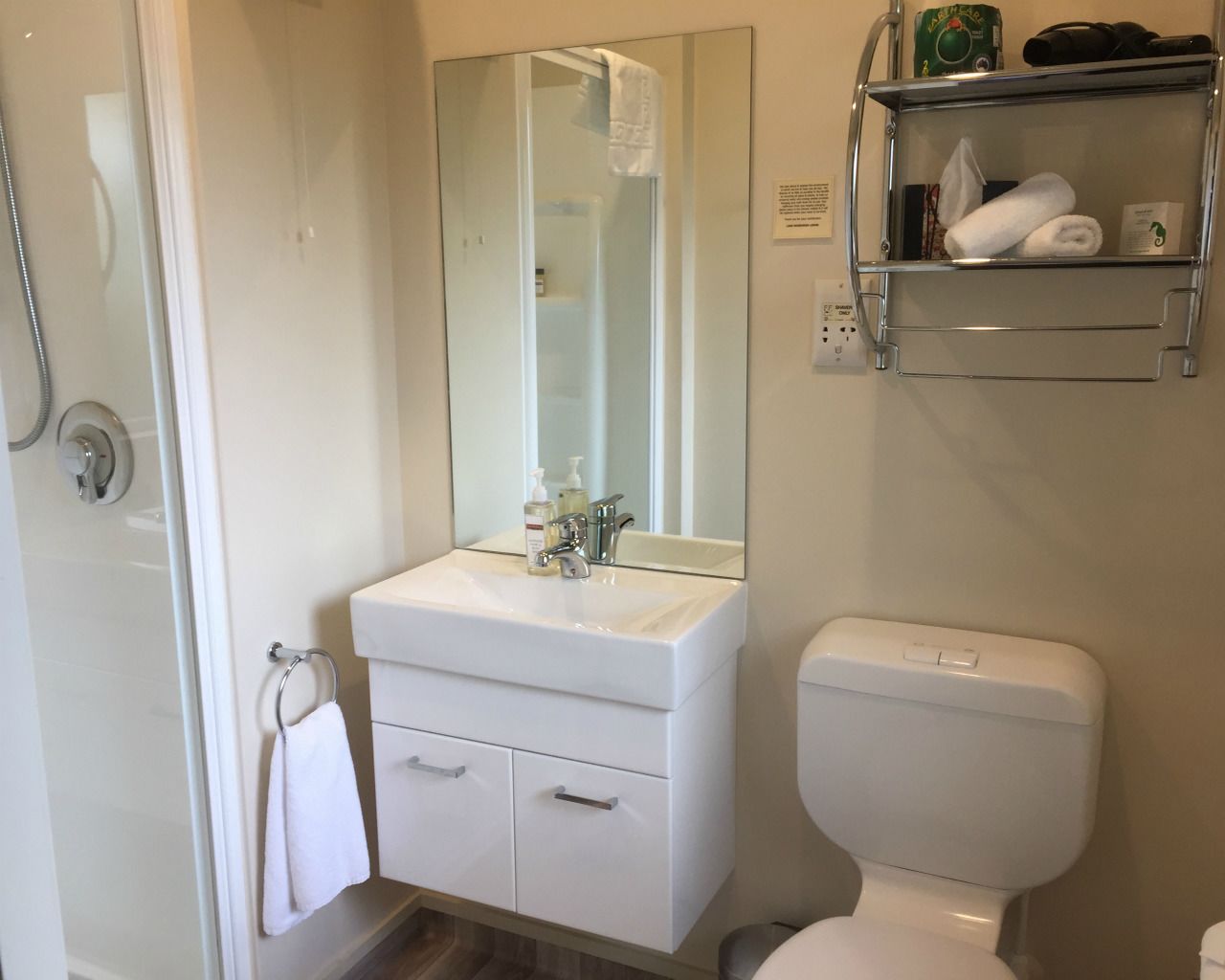 A bathroom with a white sink, mirror, and toilet. There is a towel rack with a towel hanging on it.
