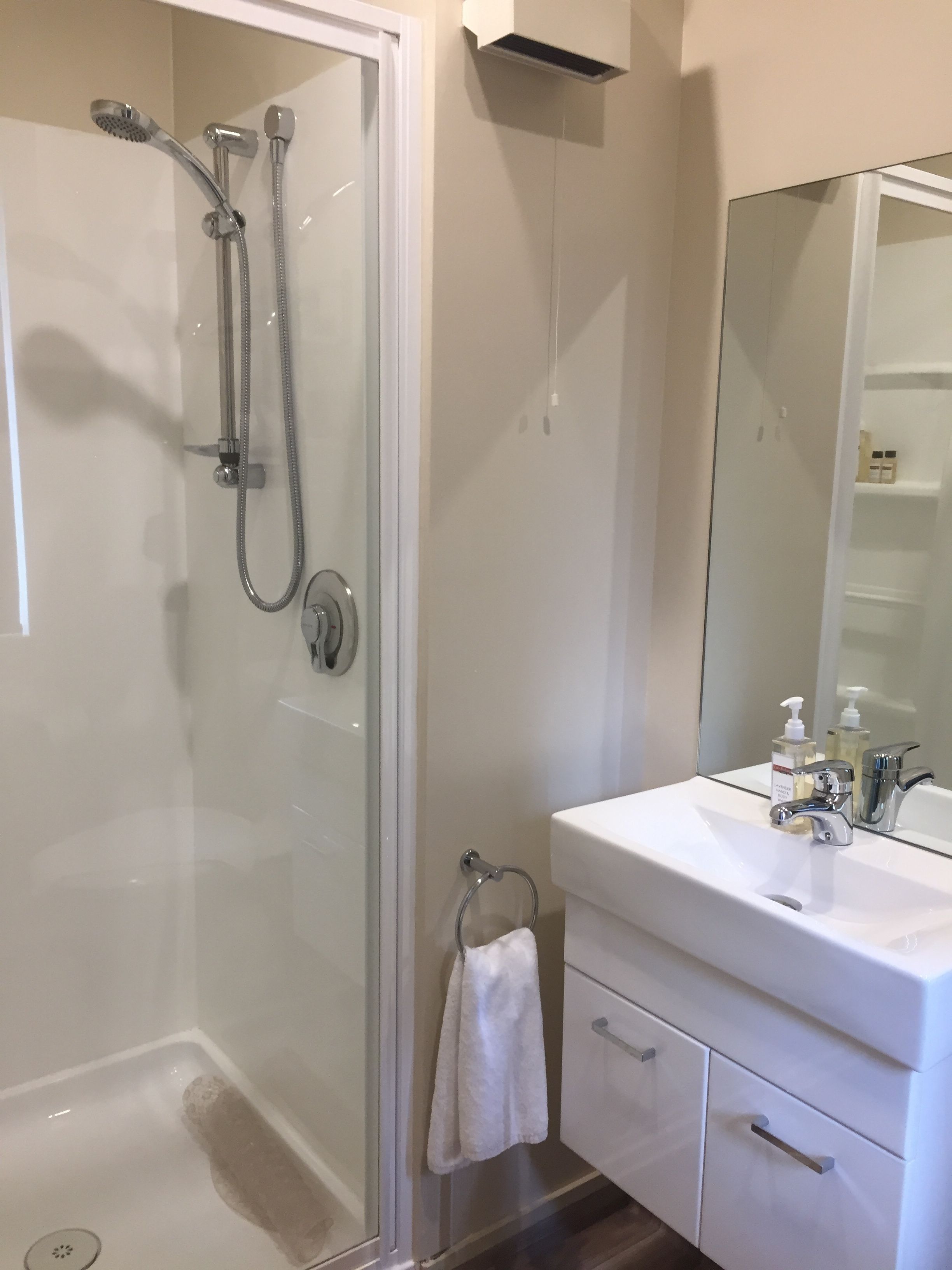 A modern bathroom with a glass-enclosed shower, a white sink with a mirror, and a towel rack.