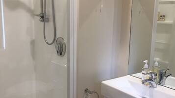 A modern bathroom with a glass-enclosed shower, a white sink with a mirror, and a towel rack.