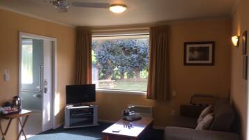 Una sala de estar con televisor, una mesita, un sofá y una ventana con cortinas.