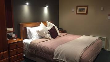 A neatly made bed with a wooden headboard, a bedside table with a lamp, and a framed picture on the wall.