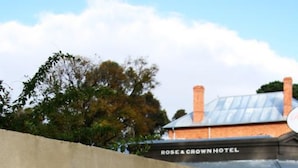 Een stenen muur met de tekst 'Rose & Crown Lodge' en een hotelgebouw op de achtergrond.