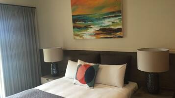 Quarto de hotel com uma cama, duas luminárias de cabeceira, um quadro na parede e uma janela com cortinas.