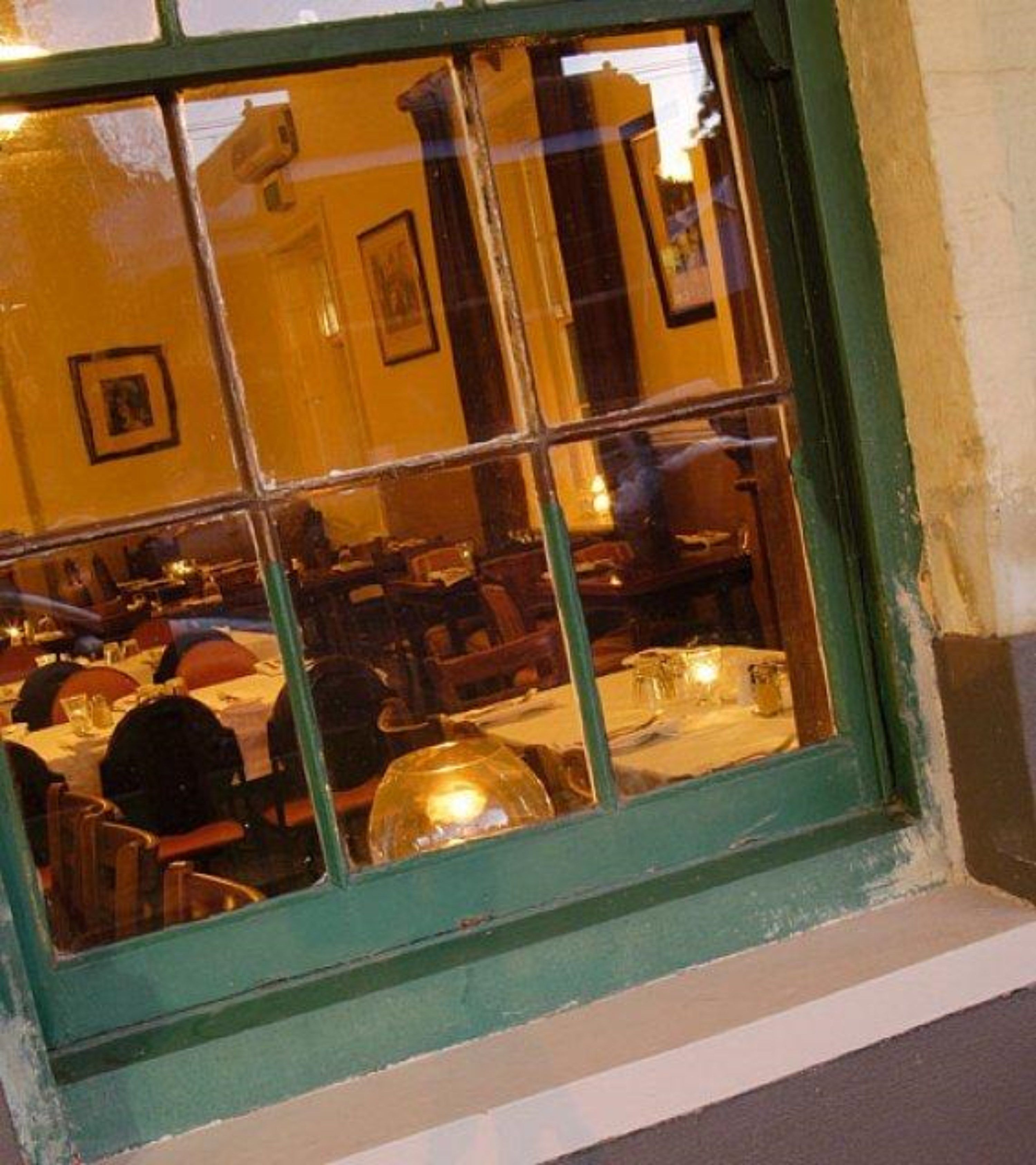 A restaurant interior with tables and chairs, a green-framed window, and a yellow wall.
