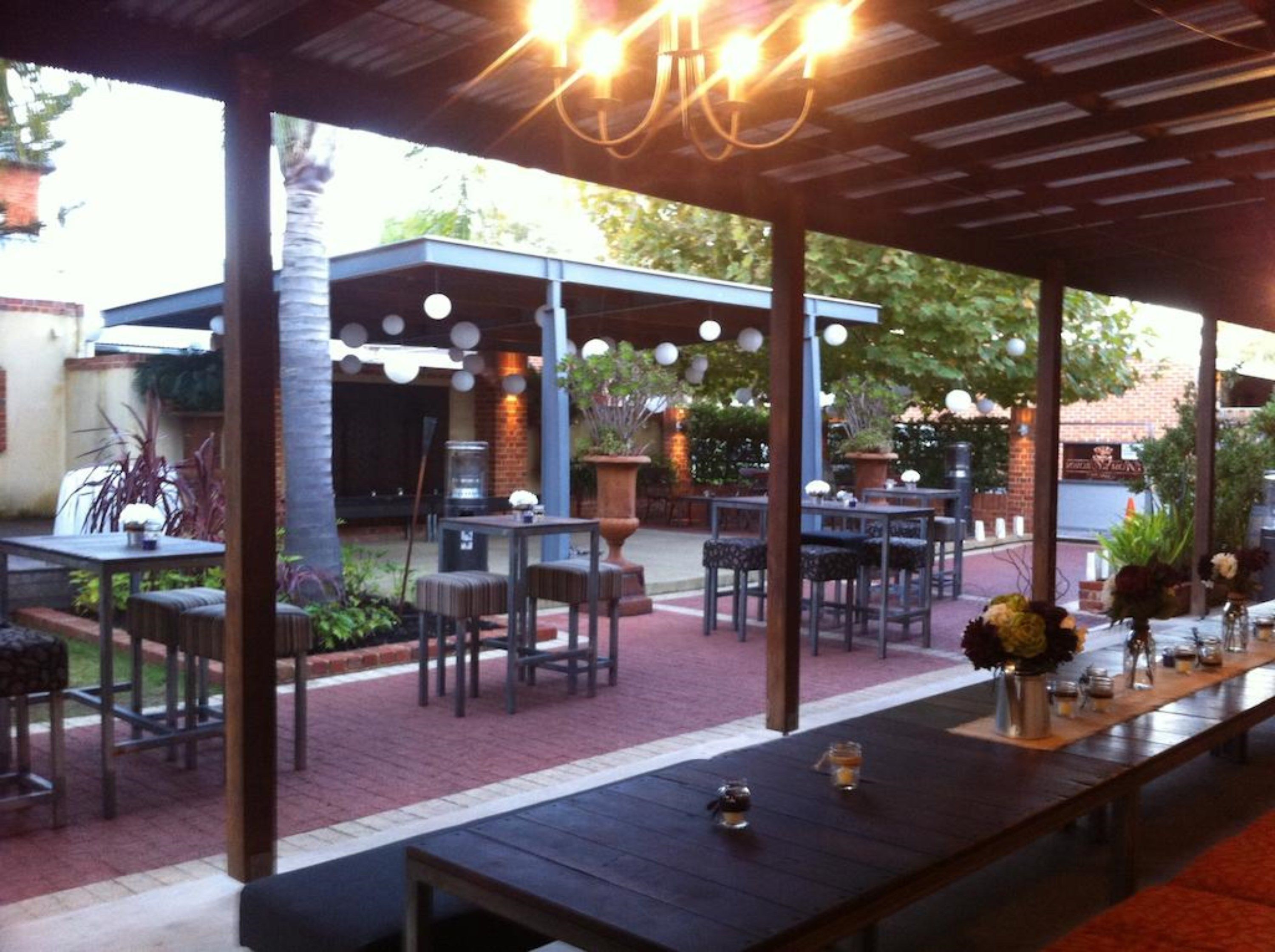 An outdoor patio area with tables and chairs, a covered seating area, and potted plants.