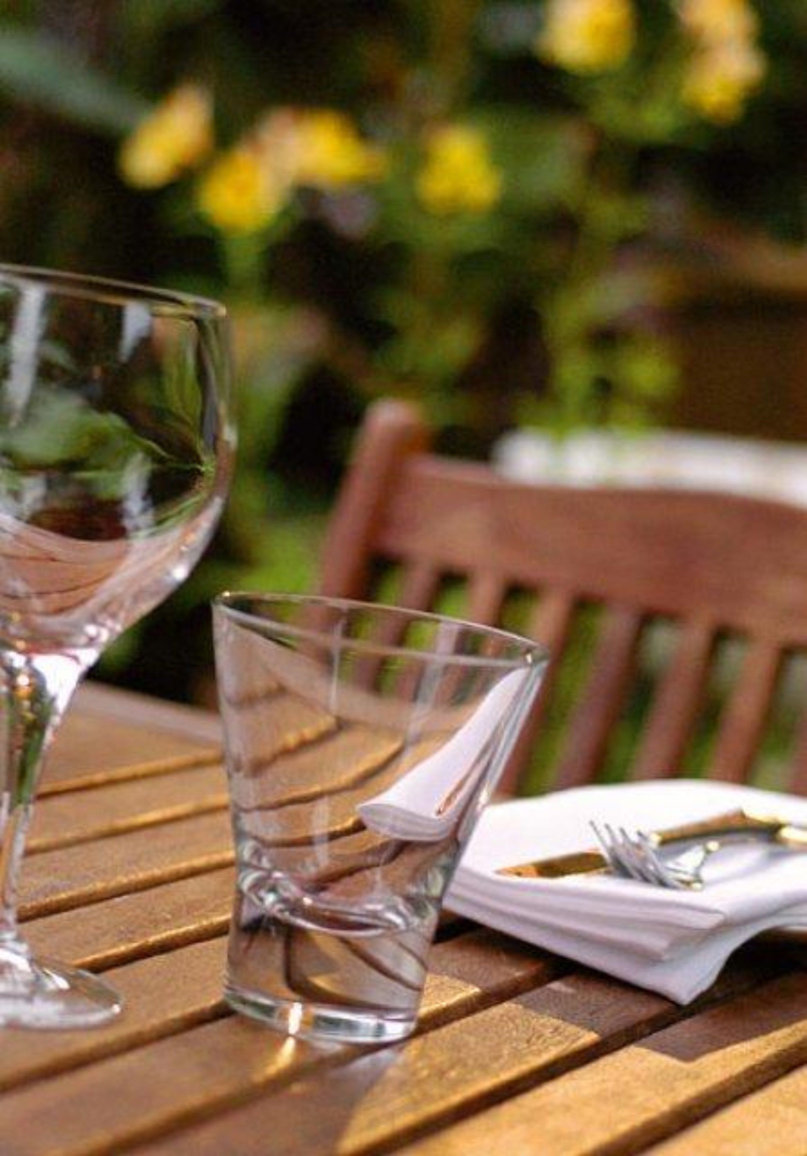A wooden table with two clear glasses and a folded napkin with cutlery.