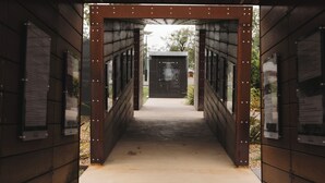 A covered walkway with metal railings and a concrete floor, leading to a building with a sign.