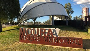 A memorial sign for the Moira Miners' Memorial with a large, white, semi-circular roof structure in the background.