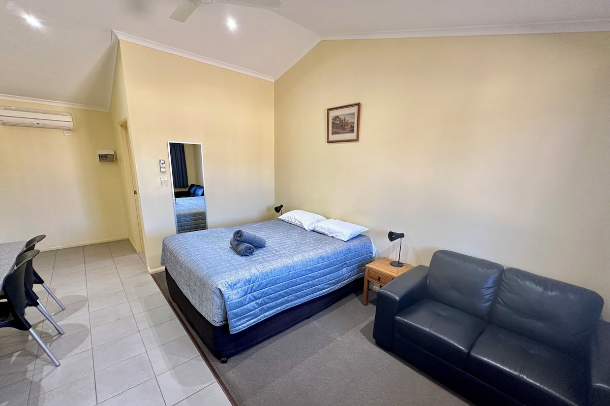A hotel room with a bed, a black leather sofa, a desk with a chair, and a ceiling fan.