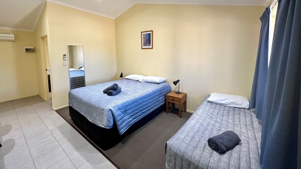 A hotel room with a large bed, a smaller bed, a nightstand, a ceiling fan, and a window with curtains.