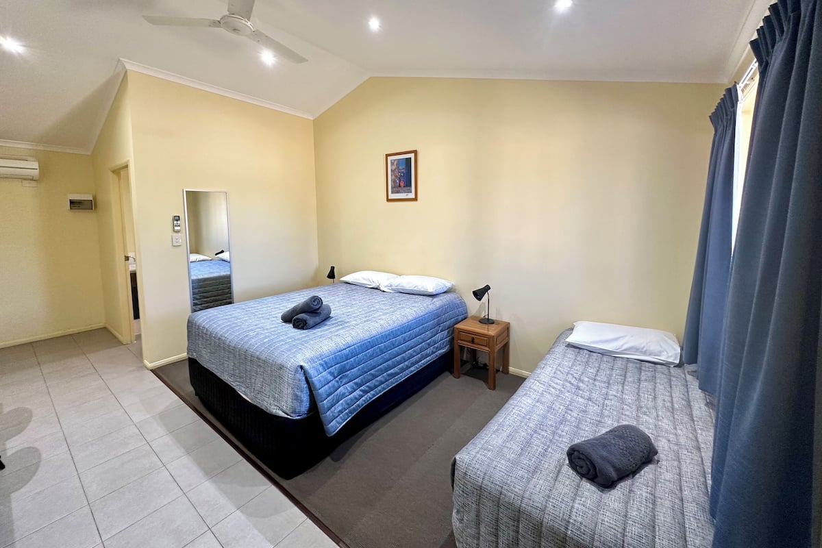 A hotel room with a large bed, a smaller bed, a nightstand, a ceiling fan, and a window with curtains.