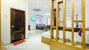 Habitación de hotel con estructura de cama de madera, televisor montado en la pared y zona de comedor con mesa y sillas.