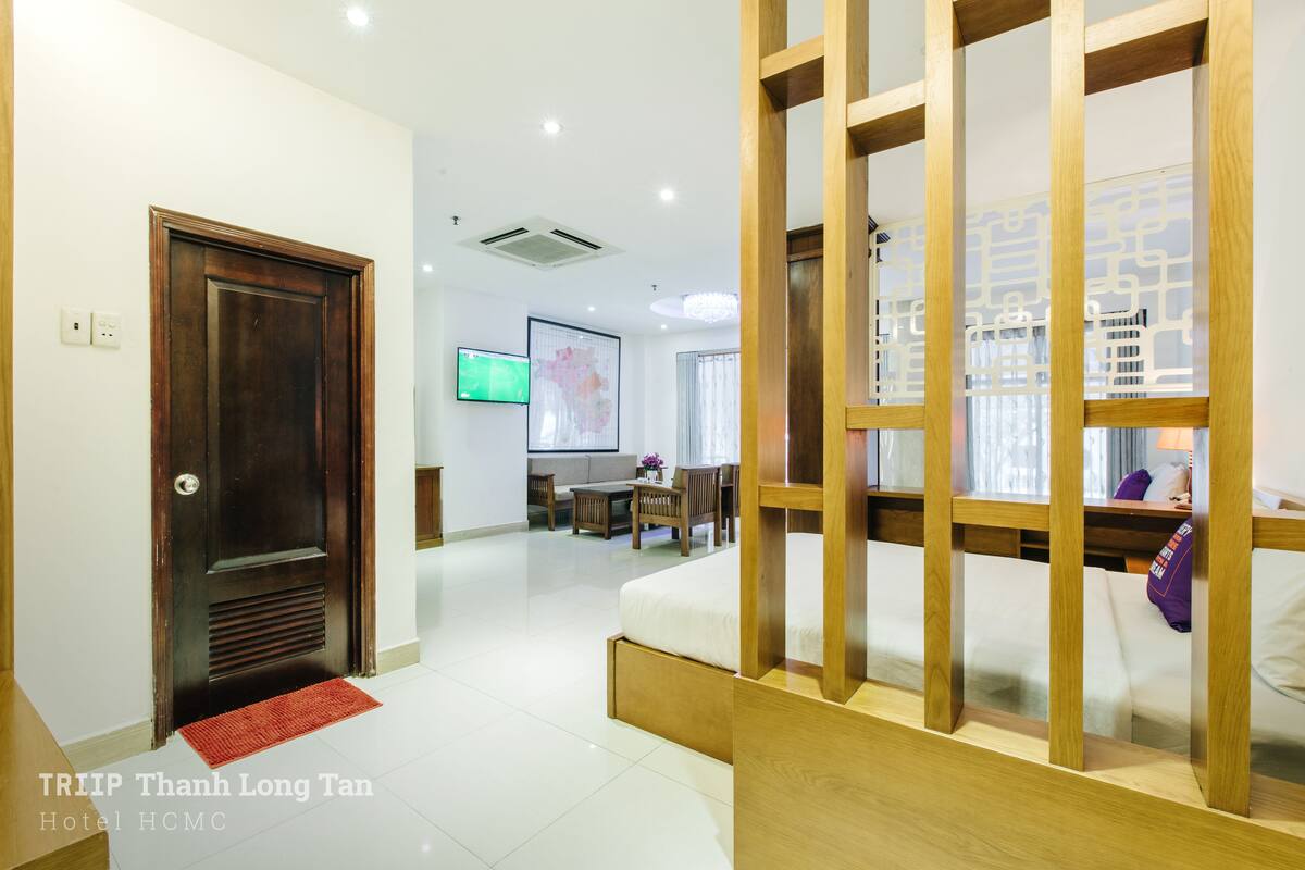 A hotel room with a wooden bed frame, a TV mounted on the wall, and a dining area with a table and chairs.