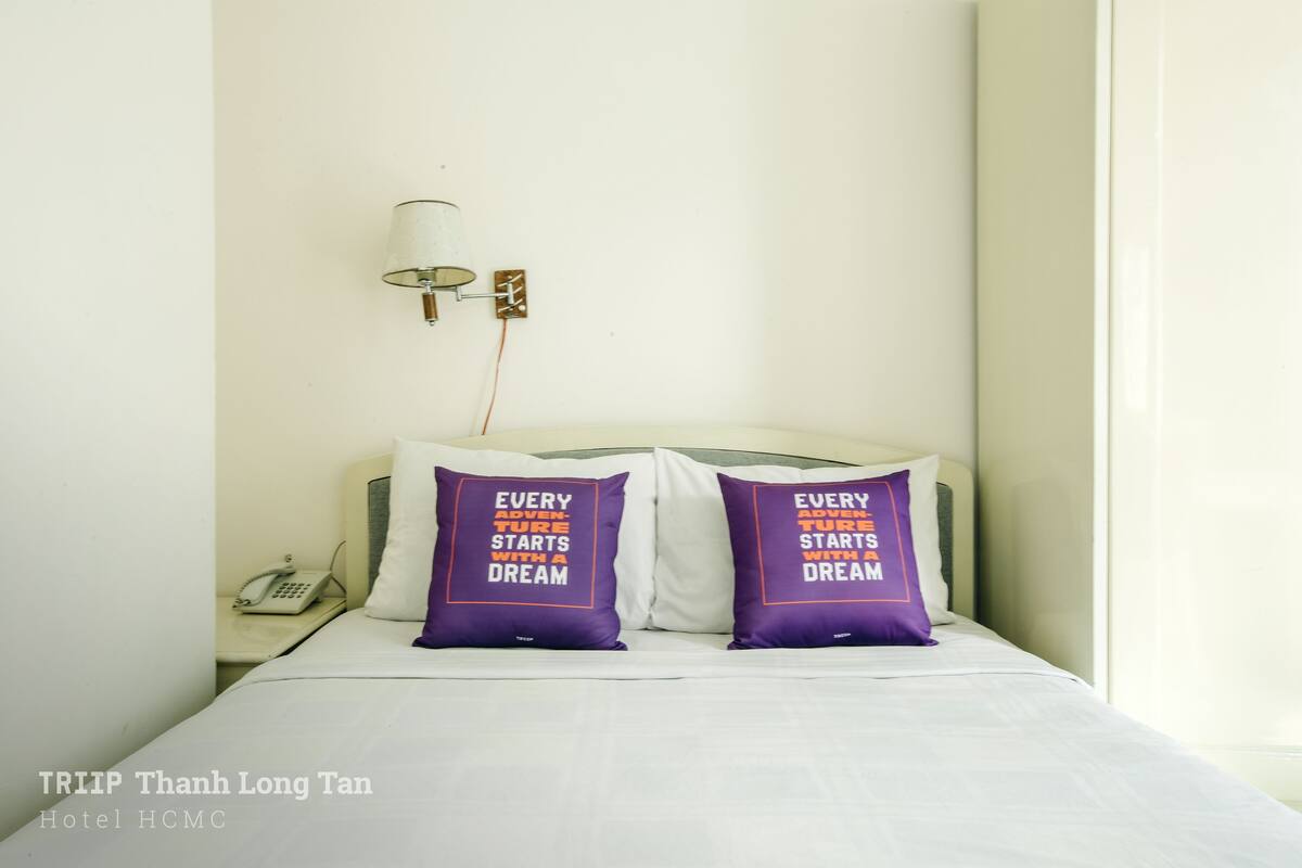 A hotel room with a bed, two pillows with motivational text, a bedside lamp, and a phone on the nightstand.
