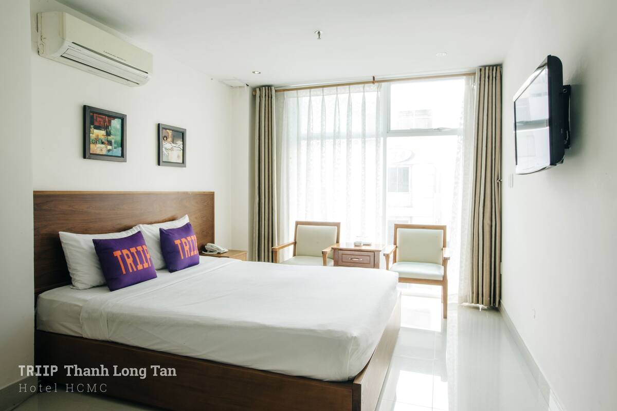 A hotel room with a large bed, a TV, and a view of the outside.