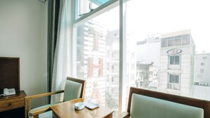 Habitación de hotel con escritorio de madera, dos sillas, teléfono y ventana con vista a edificios cercanos.