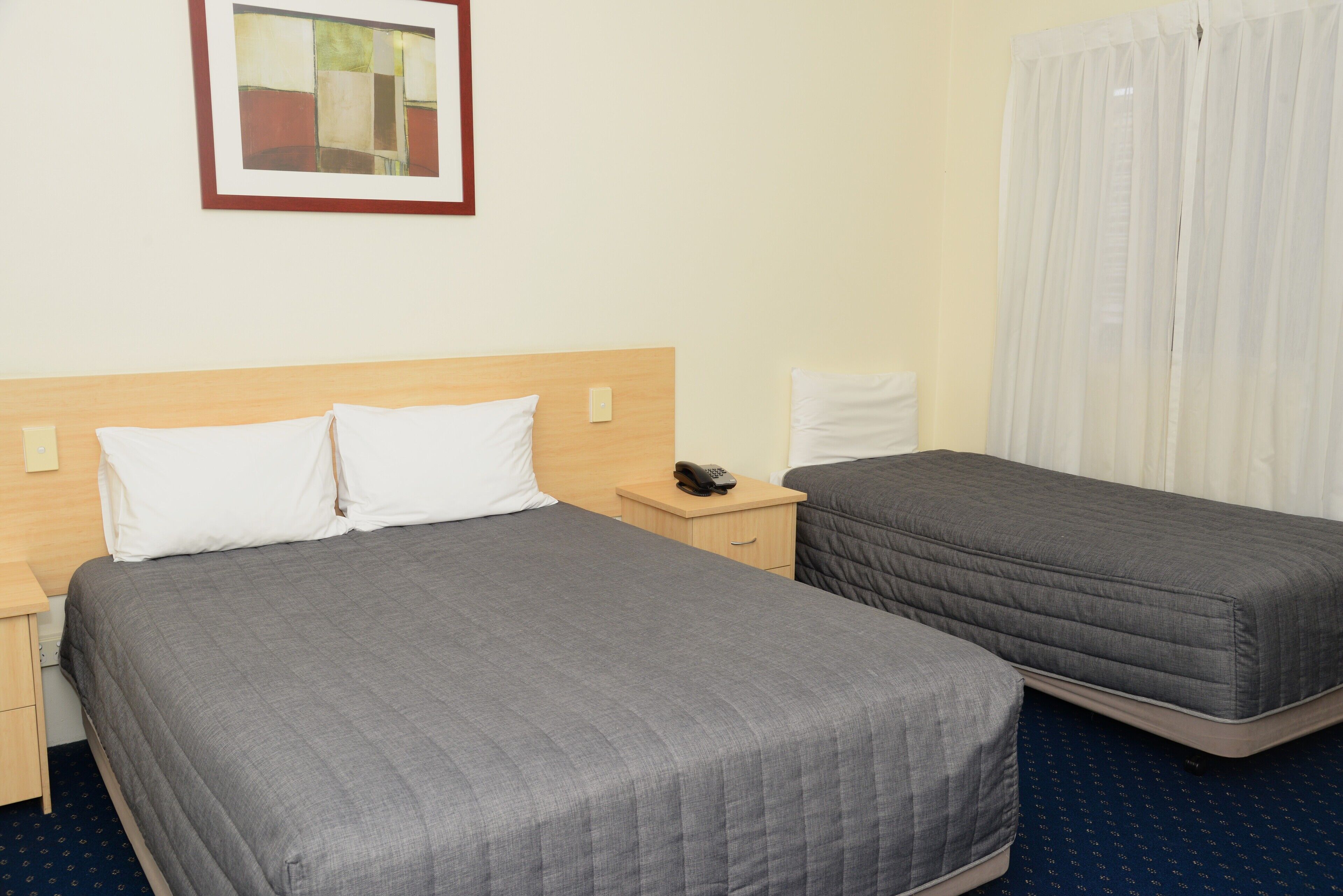 A hotel room with two beds, a bedside table with a phone, a nightstand, and a painting on the wall.