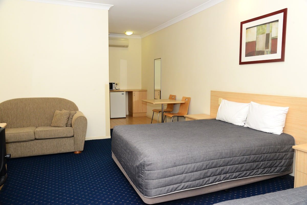 Quarto de hotel com cama, sofá, escrivaninha e cadeira.
