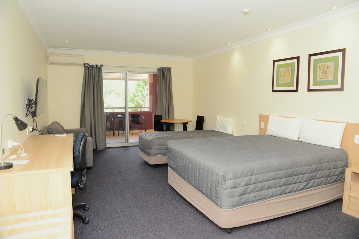 Quarto de hotel com cama, escrivaninha, cadeira e uma mesinha.