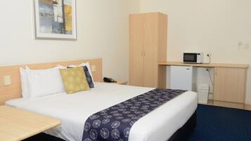 A hotel room with a bed, bedside table, a desk with a microwave, a telephone, and a cabinet.