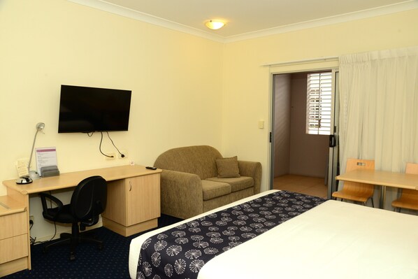 Habitación de hotel con cama, escritorio, silla, televisor y ventana con cortinas.