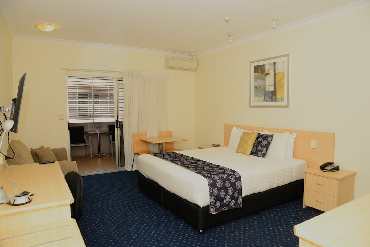 Quarto de hotel com cama, mesa de cabeceira, escrivaninha, cadeira e uma pequena mesa com uma cadeira.