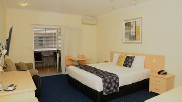 A hotel room with a bed, bedside table, desk, chair, and a small table with a chair.
