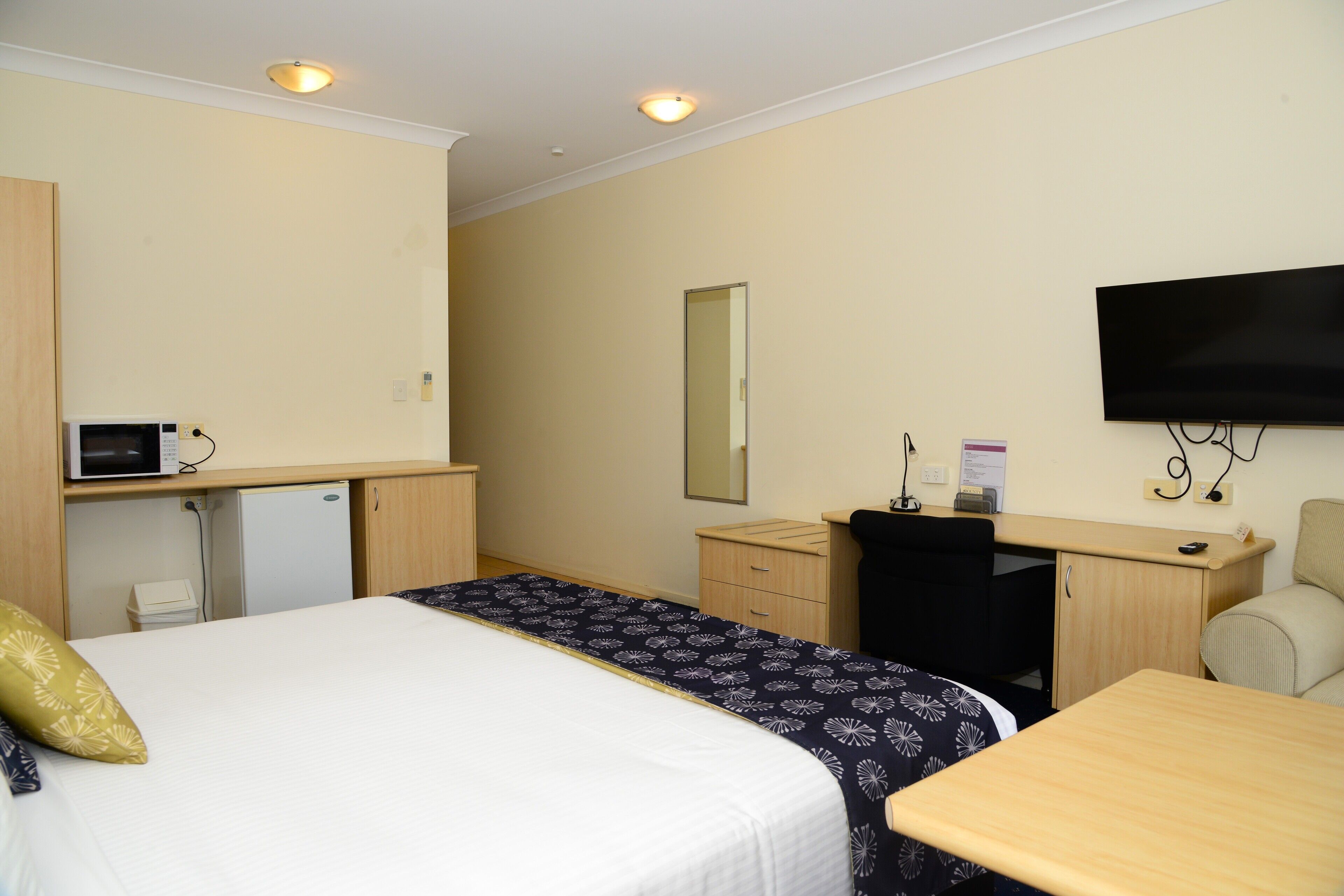 Ein Hotelzimmer mit Bett, Schreibtisch, Sessel, Fernseher und Mikrowelle.
