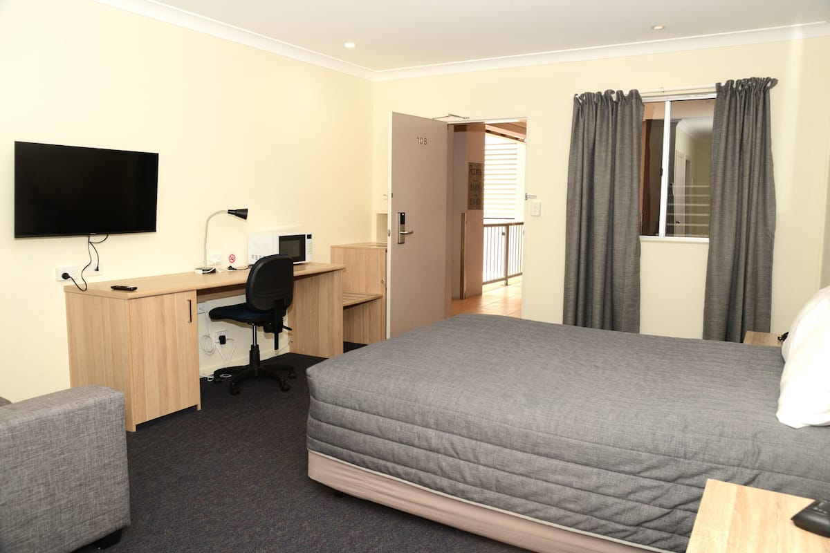 Quarto de hotel com cama, escrivaninha, cadeira, televisão e vista para o exterior.