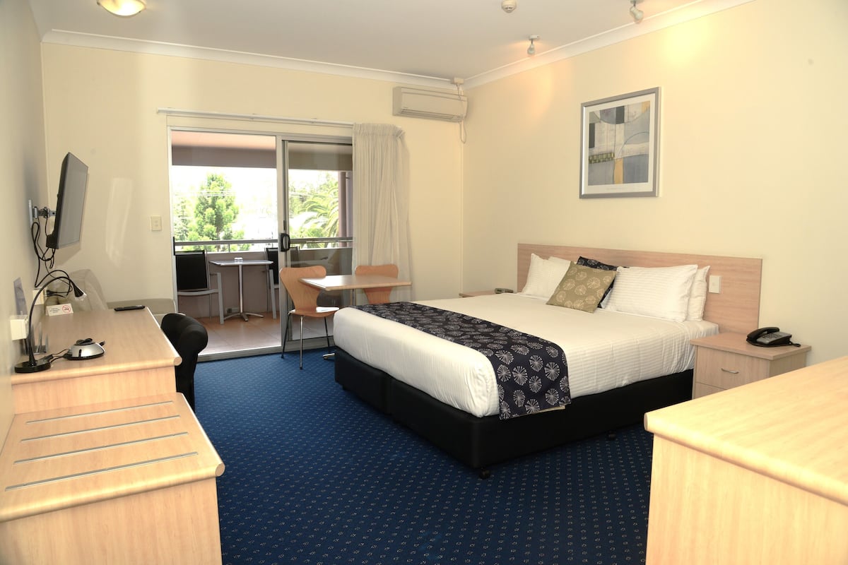 Quarto de hotel com cama, escrivaninha, cadeira e vista para o exterior.