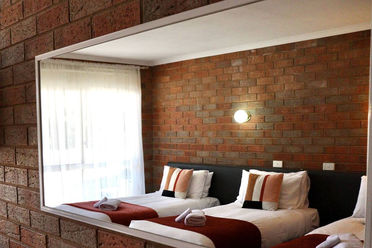 Une chambre d’hôtel avec deux lits, un mur en briques, une fenêtre avec des rideaux et un luminaire fixé au mur.