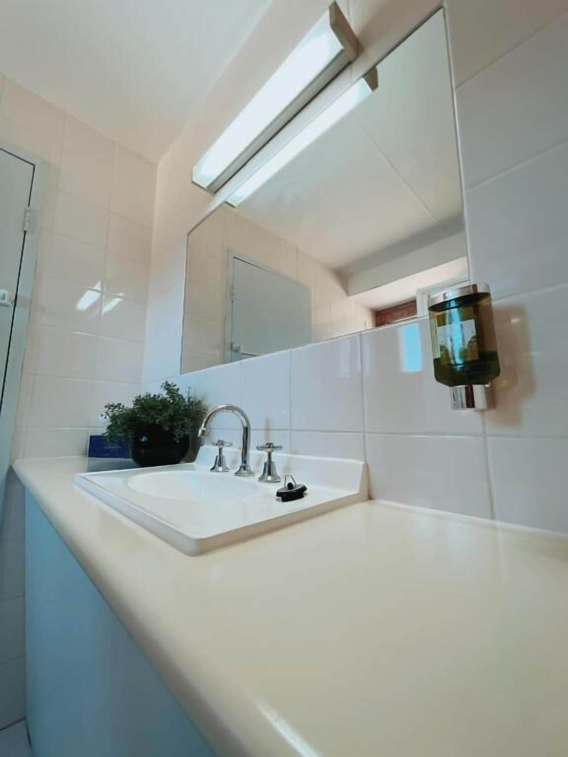 A bathroom with a white sink, a mirror, and a wall-mounted light fixture.