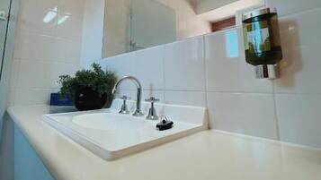 A bathroom with a white sink, a mirror, and a wall-mounted light fixture.