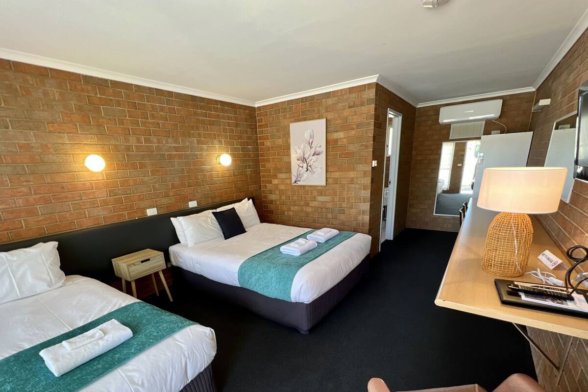 Une chambre d’hôtel avec deux lits, un bureau avec une lampe, une chaise et une salle de bain visible à travers une porte ouverte.